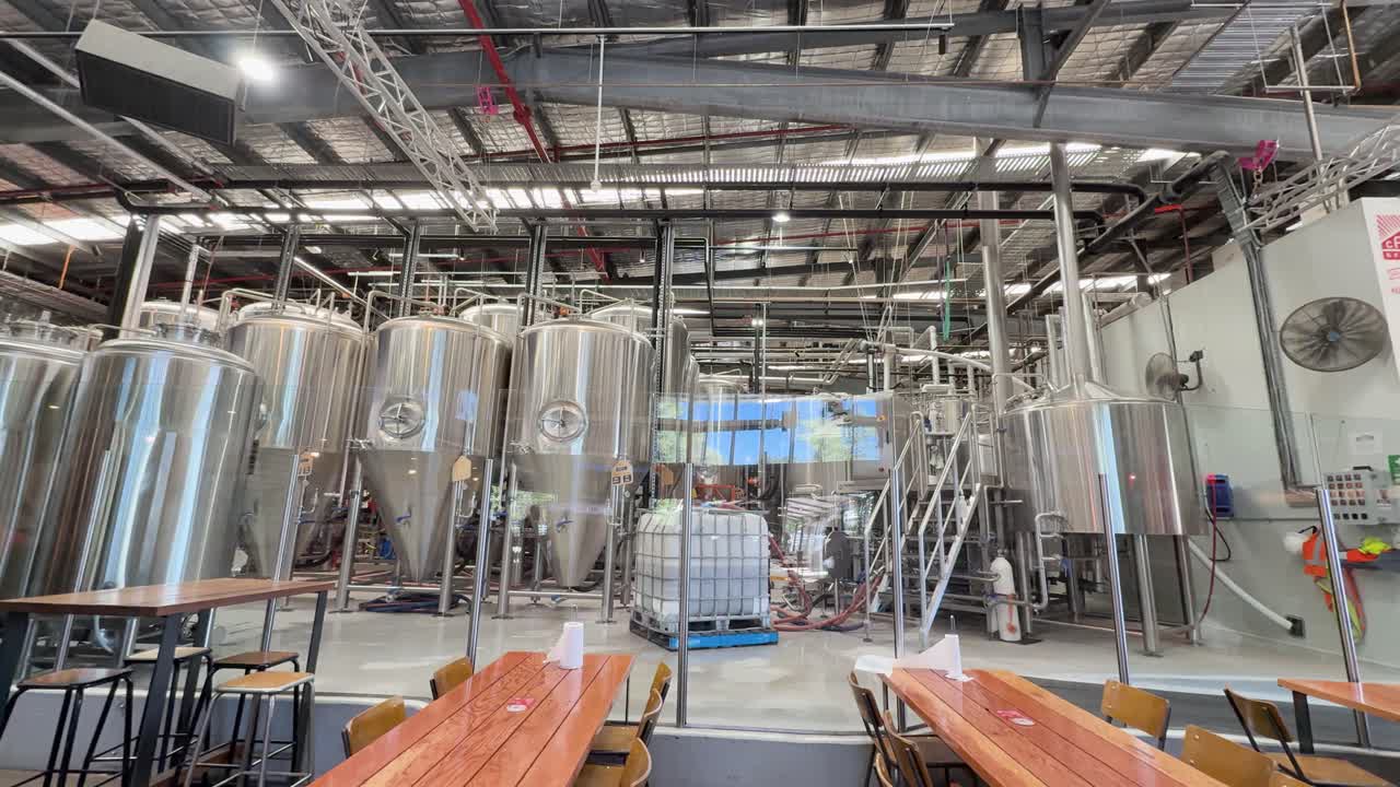 Plano amplo de uma cervejaria artesanal moderna com grandes tanques de aço inoxidável e mesas de madeira