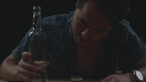 close up of drunk asian man crying and pouring vodka in a shot glass before drinking in black background