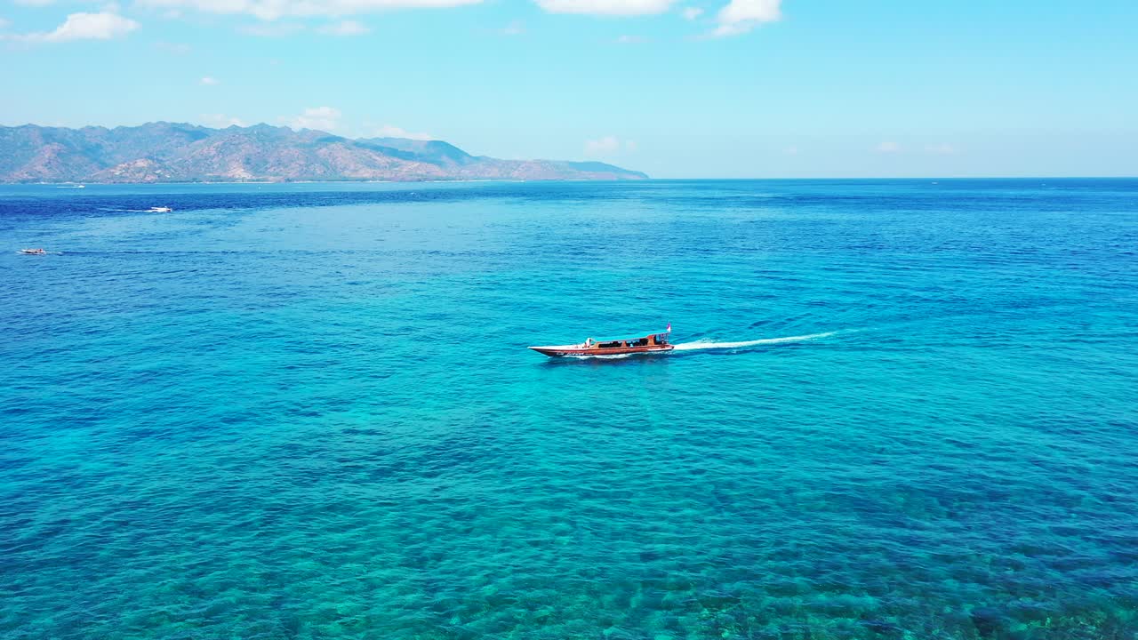 Long tail boat sailing across beautiful turquoise lagoon with coral reefs growing under clear water, bright sky with white clouds in Indonesia