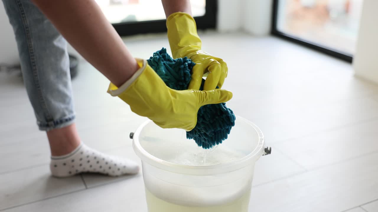 Female cleaner in rubber gloves wrings mop rag over bucket