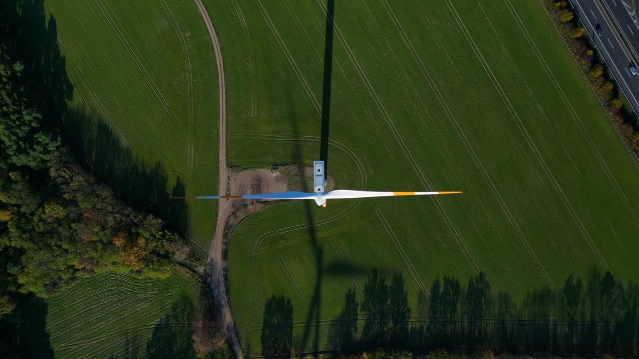 Wind turbine standing in green field next to german autobahn highway, generating renewable clean green eco friendly energy. speed ramp hyper motion time lapse vertical bird's eye view drone