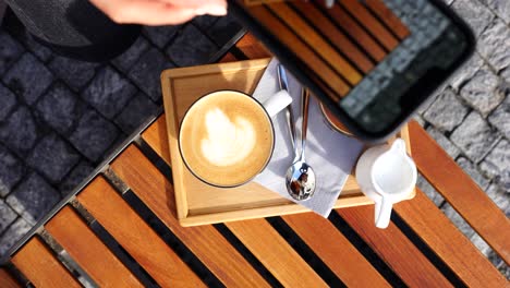 girl capture multiple photos of latte foam art on wooden outdoor table