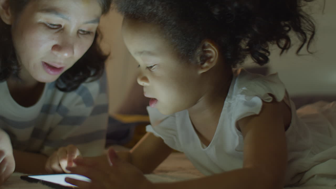Asian Little Girl and Mom Playing on Tablet in Bedroom