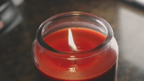 Rote-Wachskerze-Im-Glas-Mit-Schwankender-Flamme-Im-Bokeh-Hintergrund