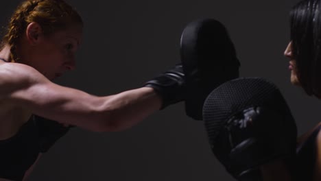 Primer-Plano-De-Una-Foto-De-Estudio-De-Dos-Mujeres-Maduras-Que-Usan-Ropa-De-Gimnasio-Haciendo-Ejercicio-De-Boxeo-Y-Sparring-Juntas-Filmadas-De-Perfil