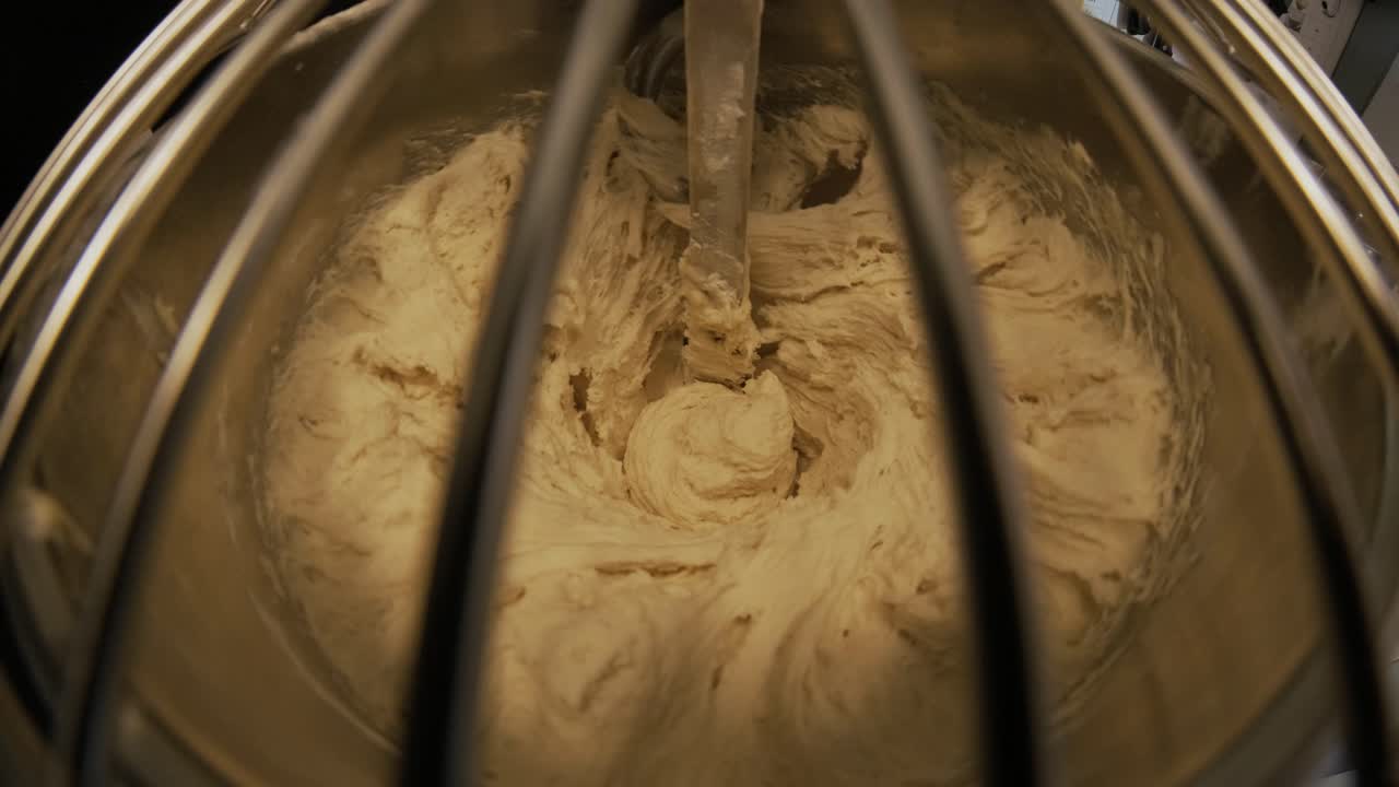 Close-up of dough mixing in a professional kneader machine in kitchen of bakery or at the manufacturing. Stock footage. Dough making process