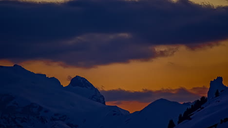 time lapse shot of grey clouds flying over snowy mountain summits during golden sunset time