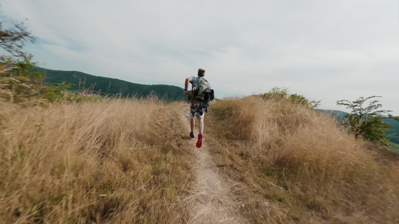 Uomo che corre, libertà, energia, sentiero escursionistico di montagna. Ripresa da drone FPV. Ragazzo felice che corre su percorso di trekking tra colline, valli e cime. Attività all'aperto nella natura, esplosione di energia, corsa sportiva atletica, periodo estivo, giornata di sole splendente.
