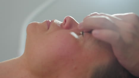 specialist massaging client nose and cheeks with gentle fingertip strokes in professional spa environment under soft clinical lighting for relaxation and skin rejuvenation during facial session