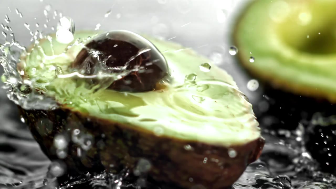 Gocce d'acqua che schizzano al rallentatore su avocado fresco e verde