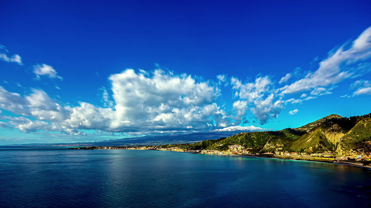 vista de ángulo alto de la pequeña ciudad de taomina en italia al lado del mar azul en un día soleado con nubes blancas pasando en timelapse