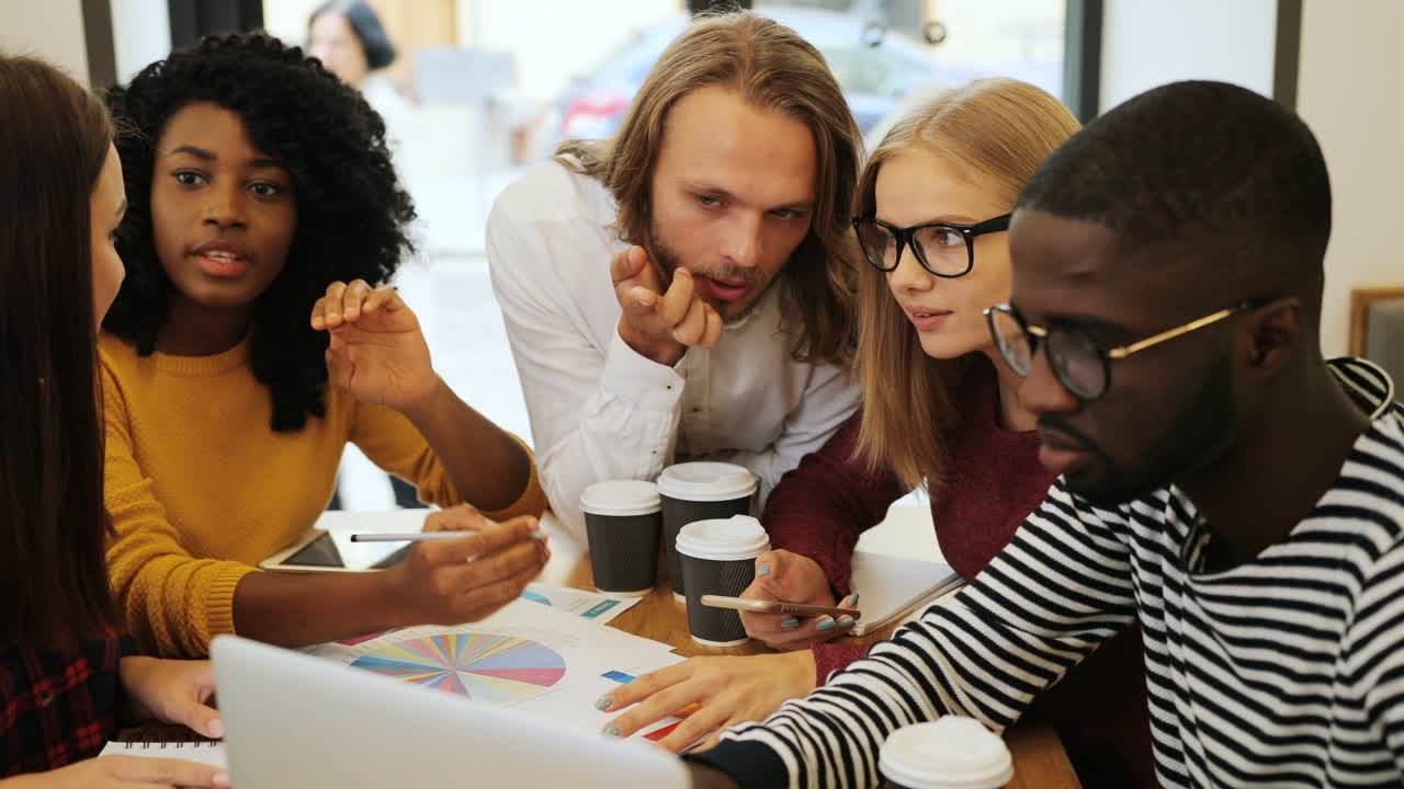 Close-up view of multiethnic coworkers viewing graphics and talking sitting at a table in a cafe
