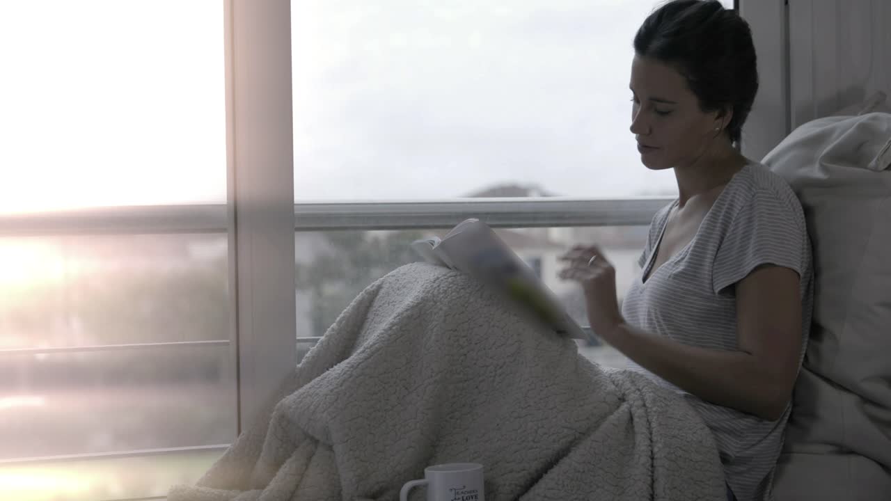 Giovane donna che legge una rivista e beve caffè vicino alla finestra