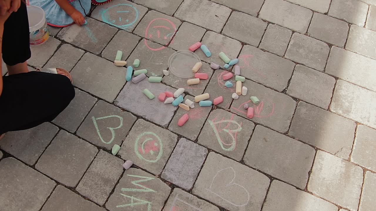 una madre y su hijo dibujan con tiza en el suelo frente a su casa