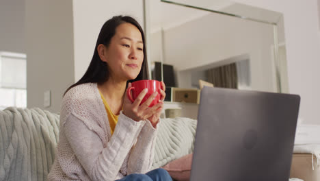 Video-of-happy-asian-woman-wit-coffee-using-laptop