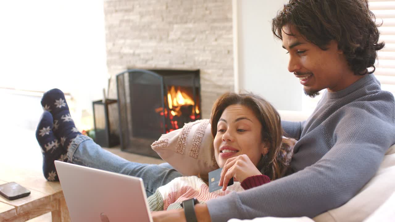 Coppia che naviga sul sito, prende la carta di credito e digita le informazioni per l'acquisto sul laptop in salotto