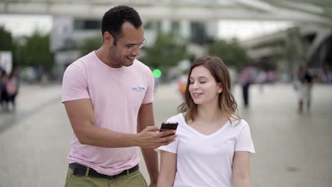 una joven pareja sonriente caminando por la calle y mirando el teléfono