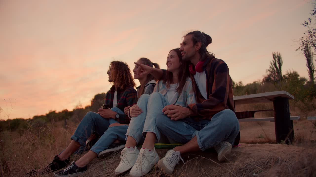 dos parejas enamoradas están sentadas en la naturaleza. dos chicos están señalando sus manos hacia adelante y hablando. descanse fuera de la ciudad contra el fondo de la puesta de sol. descanse en la casa de campo