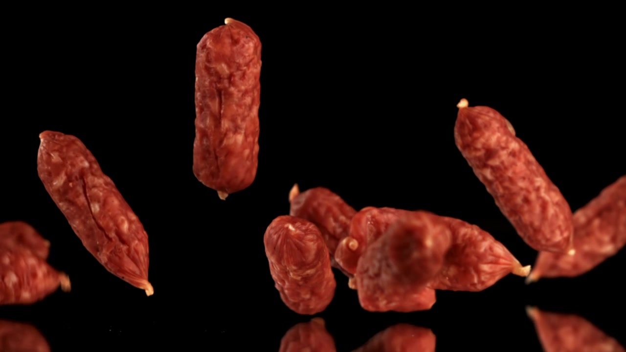 Mini salsicce di salame che cadono al rallentatore su sfondo nero.