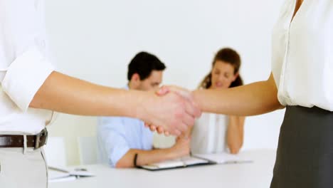 Business-people-shaking-hands-with-colleagues-behind-them