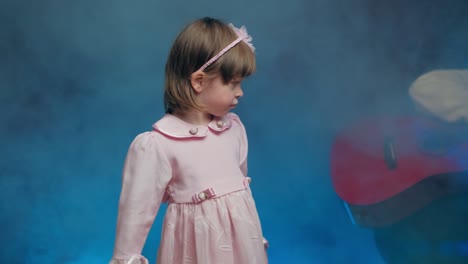 cute little girl in a pink vintage dress stands with a microphone on stage