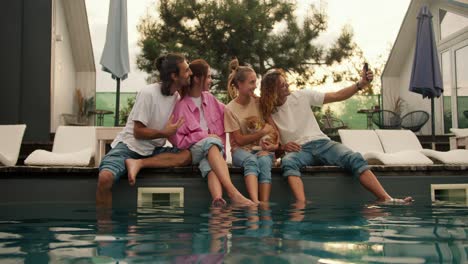 Curly-boy-in-glasses-takes-a-fun-selfie-with-his-friends-near-the-sunbeds-by-the-pool.-Rest-in-the-country-house