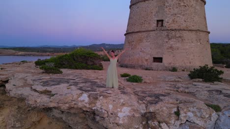 barefoot hippie girl practicing yoga at sunset near torre des carregador, ibiza, spain. fantastic aerial view flight static tripod hovering drone