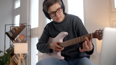 woman learning to play electric guitar at home