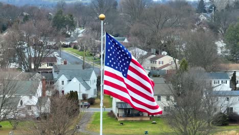 Primer-Plano-Aéreo-De-La-Bandera-Americana-Ondeando-Sobre-Casas-De-Barrio-Suburbano