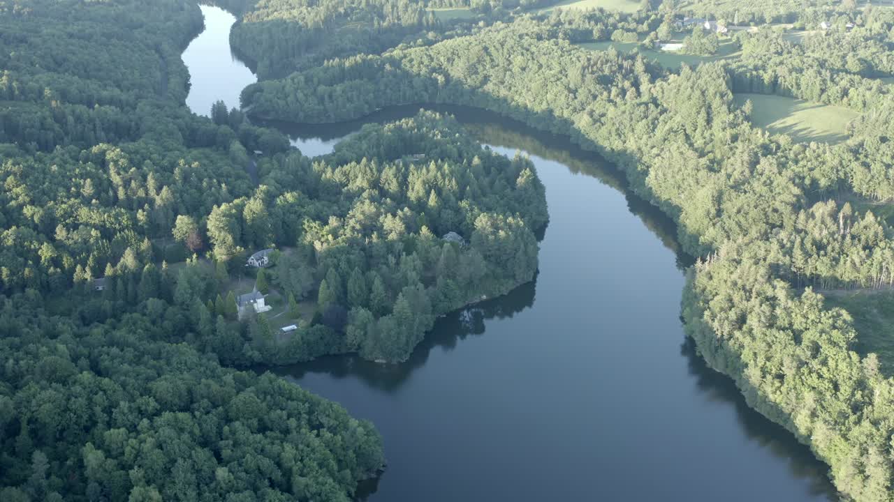 Aerial view of vast winding river or lake surrounded by dense green forest landscape, Marcillac La Croisille, France