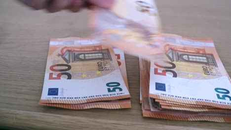 Close-up-shot-of-the-hands-of-a-rich-man-calculating-or-counting-fifty-euro-notes-keeping-it-on-the-table-in-two-hierarchy-sides,-Foreign-currency-saving-money-concept