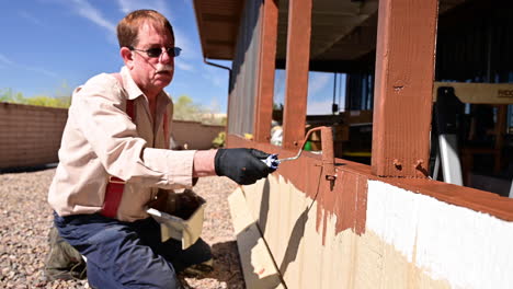 elderly man painting patio wood with brown paint outside - close up