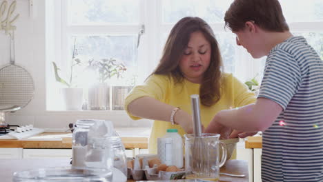 young downs syndrome couple mixing ingredients for cake recipe they are baking in kitchen at home