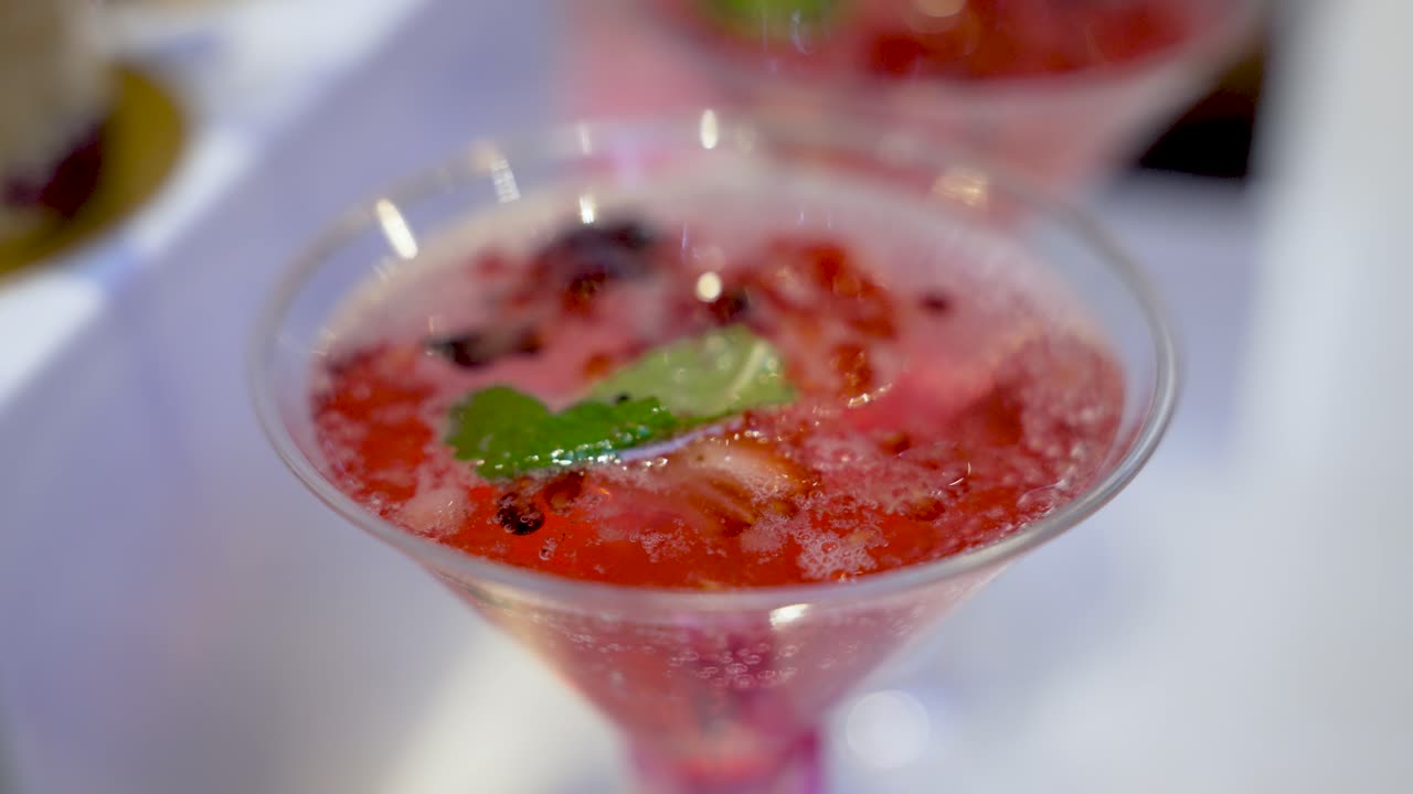 Nærbillede af en forfriskende, rød frugtcocktail i et martiniglas, pyntet med mynte
