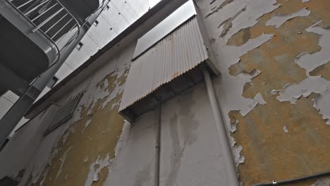 a weathered urban wall features peeling white paint over a yellow base and an old, corrugated metal panel, showcasing urban decay and texture.