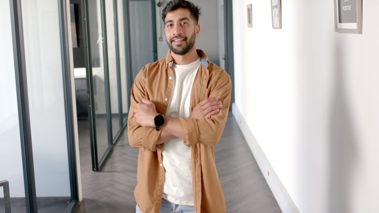 Smiling man in office hallway crossing arms, wearing casual shirt and smartwatch