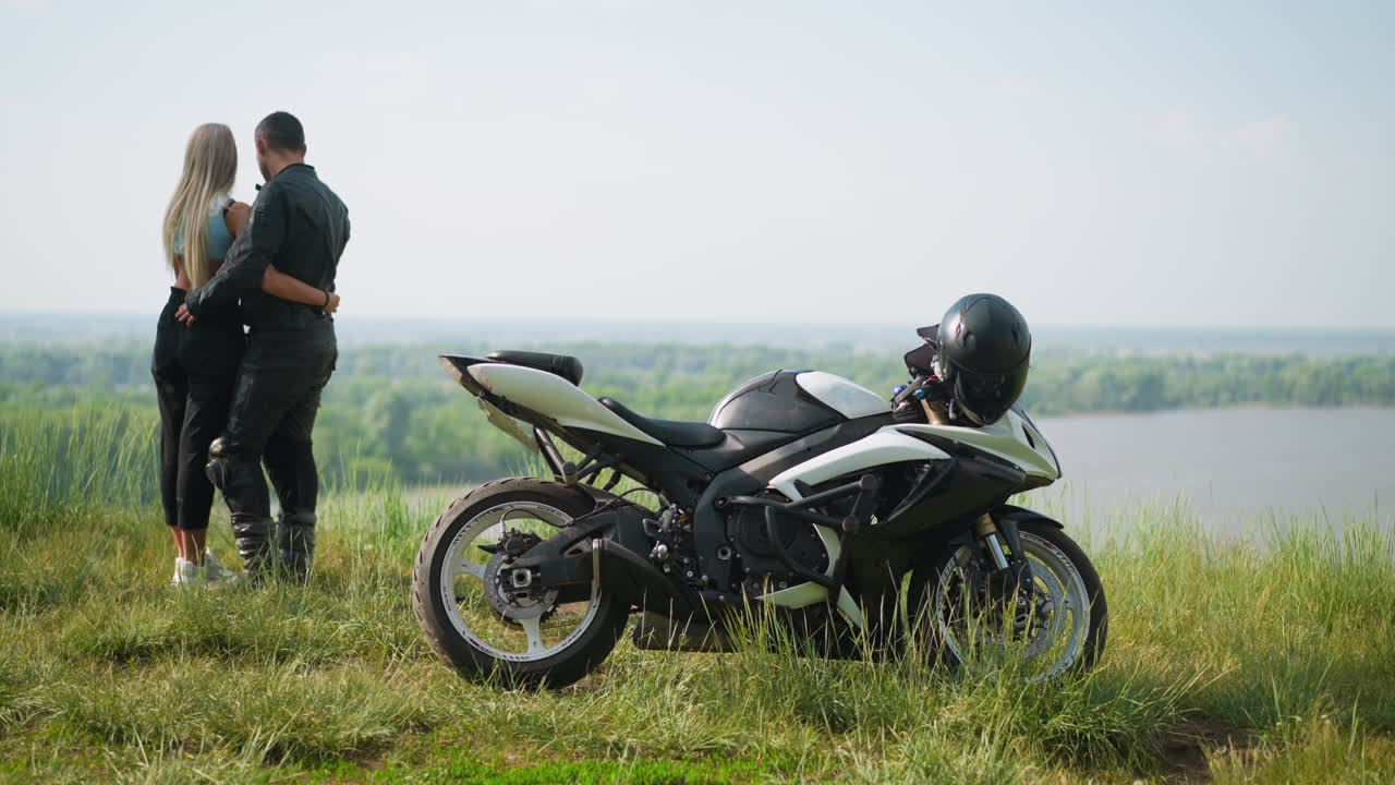 мотоциклист и его подруга стоят рядом с велосипедом на холме возле озера