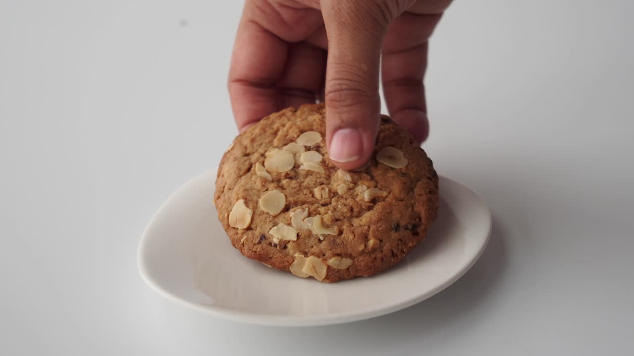 mano alcanzando una galleta de avena en un plato blanco