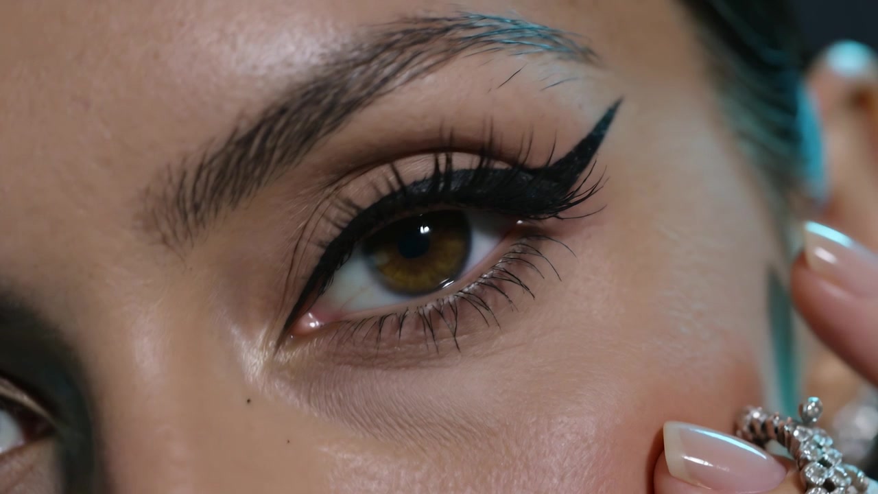 Opening close-up, woman's right eye blinking while nails touching cheek, showing eyeliner and ring