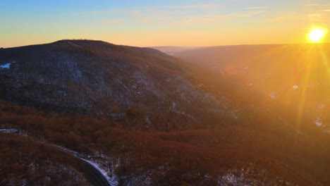 drone flying high over snow-covered mountains and a valley during sunset in winter