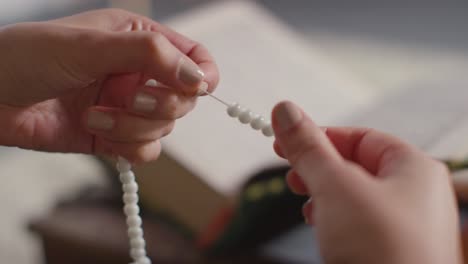 Close-Up-Of-Muslim-Woman-Praying-Holding-Prayer-Beads-With-Copy-Of-Quran-In-Background