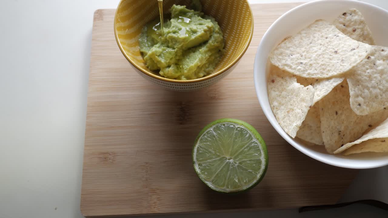 Fresh guacamole, lime, and tortilla chips on wooden board, ready for snacking indoors