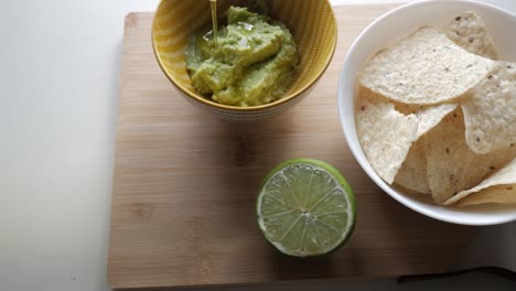 fresh guacamole, lime, and tortilla chips on wooden board, ready for snacking indoors
