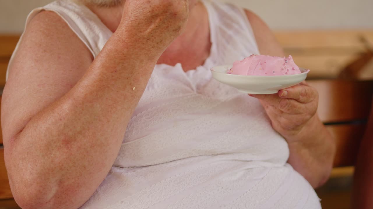 señora mayor comiendo pastel de cumpleaños rosa anónimo durante el verano
