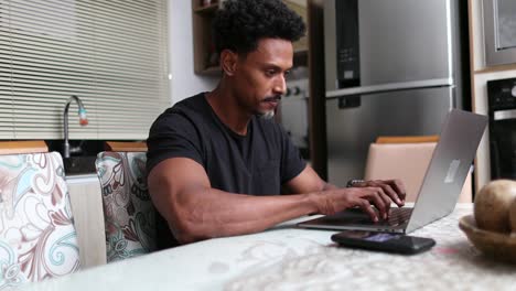 african man typing on computer laptop at home kitchen