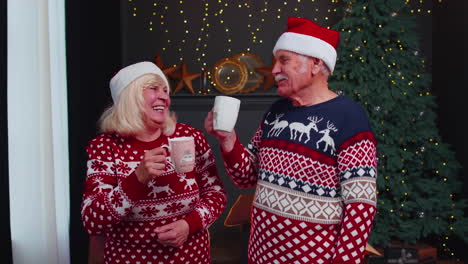 Senior-old-wife-and-husband-talking,-drinking-tea-near-glowing-xmas-tree-on-Christmas-in-home-room