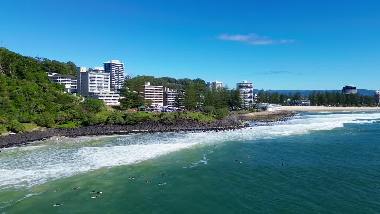 Stunning side drone video of Burleigh Head capturing the national park, sunset poin and golden beach while surfers enjoy the waves