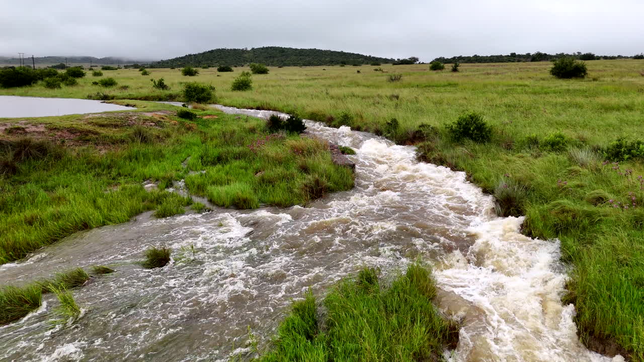 Overflowing sluice waterway surrounded by lush green landscape during rainy weather
