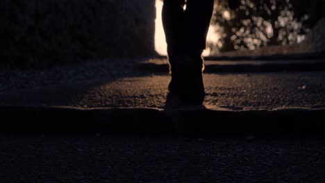 Beine-Eines-Jungen-Mannes,-Der-In-Zeitlupe-In-Frankreich-Auf-Einer-Kopfsteinpflasterstraße-Dem-Sonnenuntergang-Entgegengeht,-Mit-Sommerstimmung-Und-Einer-Kamera-In-Der-Hand-In-Der-Nähe-Einer-Kirche