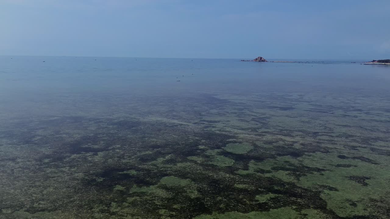 Drone circles beach while ascending, revealing mirrorlike sea and distant horizon on a calm, windless day along Vietnam’s stunning coastline.
